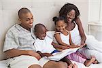 Happy family lying on bed reading book at home in the bedroom