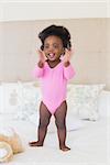 Baby girl in pink babygro standing on bed at home in the bedroom