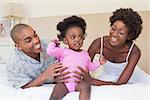 Happy parents playing with baby girl on bed together at home in the bedroom