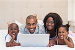 Happy family using laptop together on bed at home in the bedroom