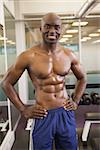 Portrait of a smiling shirtless muscular man with hands on hips in gym