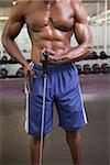 Mid section of shirtless young muscular man using resistance band in gym