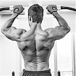 Rear view of a male body builder doing pull ups at the gym