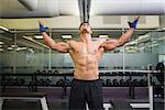 Shirtless bodybuilder with arms raised standing in gym