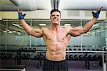 Shirtless bodybuilder with arms raised shouting in the gym