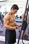 Side view of a shirtless young muscular man using triceps pull down in gym