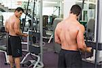 Rear view of a shirtless young muscular man using triceps pull down in gym