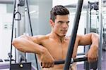 Portrait of a shirtless young muscular man using biceps pull up in gym