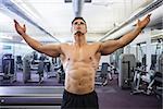 Shirtless bodybuilder with arms raised standing in gym