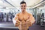Portrait of a smiling shirtless muscular man giving thumbs up in gym