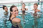 Smiling female fitness class doing aqua aerobics in swimming pool at the leisure centre