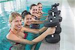 Female fitness class doing aqua aerobics with foam dumbbells in swimming pool at the leisure centre