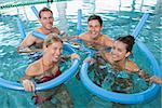 Happy fitness class doing aqua aerobics with foam rollers in swimming pool at the leisure centre