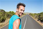 Fit man jogging on the open road smiling at camera on a sunny day