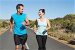 Fit happy couple jogging on the open road together on a sunny day