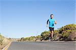 Athletic man jogging on the open road on a sunny day