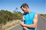 Athletic man adjusting his music player on a run on a sunny day