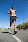 Athletic man jogging on open road with monitor around chest on a sunny day