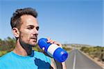 Athletic man on open road taking a drink on a sunny day