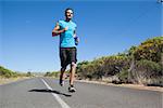 Athletic man jogging on open road holding bottle on a sunny day