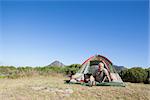 Happy camper cooking on camping stove outside his tent on a sunny day