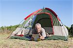 Happy camper looking at map lying in his tent on a sunny day