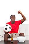 Football fan in red jersey sitting on couch cheering on white background