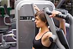 Athletic brunette using weights machine for arms at the gym