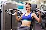 Fit smiling brunette using weights machine for arms at the gym