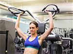 Fit focused brunette using weights machine for arms at the gym