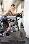 Fit brunette working out on the exercise bike at the gym