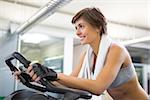 Fit smiling woman working out on the exercise bike at the gym