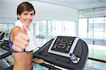 Fit brunette smiling at camera on the treadmill showing thumbs up at the gym