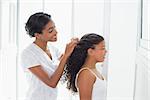 Pretty mother tying her daughters hair back at home in bathroom