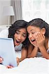 Surprised mother and daughter using tablet together at home in bedroom