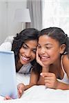 Happy mother and daughter using tablet together at home in bedroom