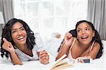 Mother and daughter reading book and listening to music together on bed at home in bedroom