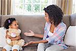 Pretty mother sitting on couch with petulant daughter at home in the living room