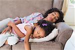 Pretty mother sleeping with her daughter on the couch at home in the living room