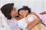 Cute daughter sleeping with mother on the sofa at home in the living room