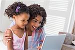 Cute daughter using laptop at desk with mother at home in the living room