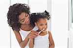 Pretty mother helping her daughter brush her teeth at home in the bathroom