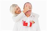 Older woman covering her partners eye while holding present on white background