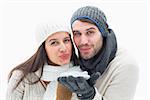Attractive young couple in warm clothes blowing on white background