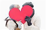 Attractive young couple in warm clothes holding red heart on white background
