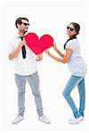 Hipster couple smiling at camera holding a heart on white background