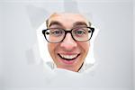 Geeky hipster smiling through hole on white background