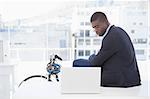 Serious businessman sitting on desk looking at laptop in his office