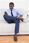 Handsome businessman sending text on sofa at home in the living room
