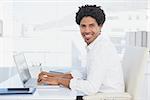 Handsome casual businessman smiling at camera working on laptop in his office